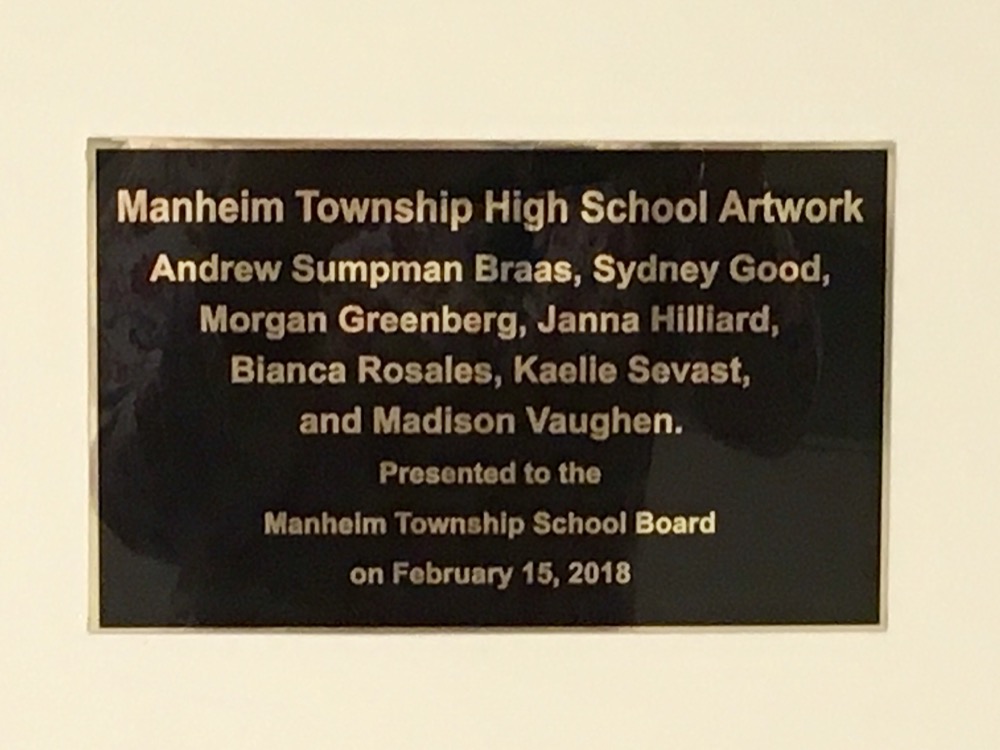 The plaque celebrating the MTSD Mural. The plaque reads: Manheim Township High School Artwork. Andrew Sumpman Braas, Sydney Good, Morgan Greenberg, Janna Hilliard, Bianca Rosales, Kaelie Sevast, and Madison Vaughen. Presented to the Manheim Township School Board on February 15, 2018