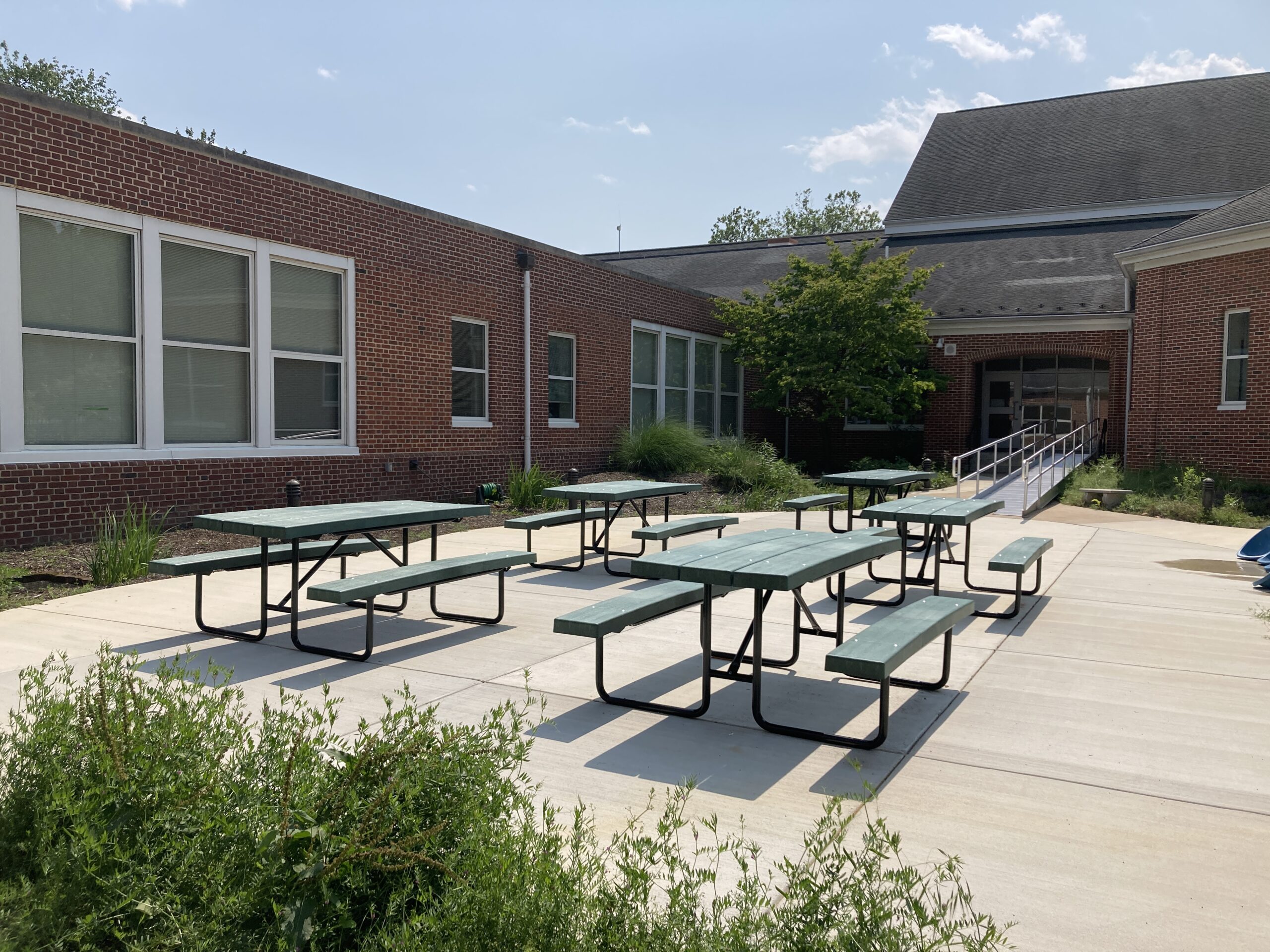 Schaeffer outdoor classroom, five picnic tables in the sunlight with a ramp leading into the school